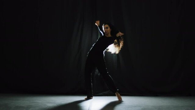 Female silhouette of dancer girl graceful hard-working performer elegant woman with long hair dancing on black studio background in darkness modern dance elements active rhythm movement body move
