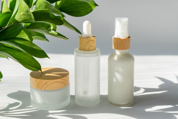 Moisturizer cream jar, serum in glass bottle on white background with green leaves with copy space. Set for skin and body care beauty products. unbranded package, showcase
