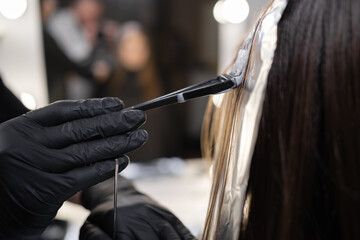 close-up side view of a strand of female hair on a special sheet of foil, the master applies hair...