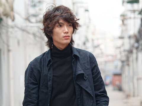 Portrait of handsome Chinese young man in black looking away with narrow street background, front view of confident young man.