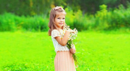 Portrait of cute little girl child with wildflowers in summer park