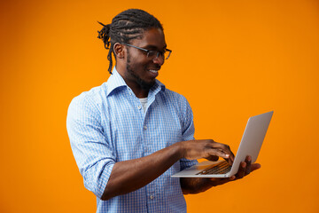 Young smiling african man standing and using laptop computer over yellow background