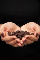 Hands of a young woman holding pieces of dark chocolate. Chocolate chips for homemade baking and cocoa.