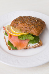 Closeup of homemade sandwich with slice of salmon, fresh lettuce leaf, cream cheese and lemon. Healthy food for family.