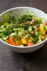 Closeup of chopped organic garden vegetables in a white bowl: tomatoes, cucumbers, yellow pepper, lettuce leaves and dill. Healthy nutrition. Cook at home.