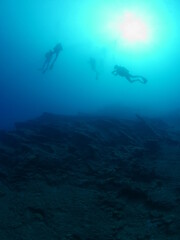 scuba divers under the boat coming up sun beam and sun ray on the surface underwater ocean scenery ascending descending