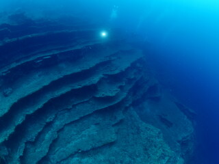 scuba divers around a reef underwater deep blue water big rock 
