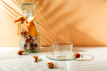 Beautiful transparent glass mason jar with orange bow and few caramels on light background.