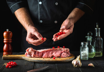 The chef prepares raw calf meat In the kitchen. Before baking, the cook puts the viburnum on the beef. National dish