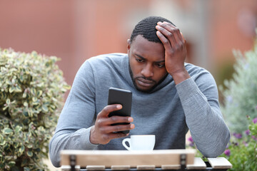 Worried man with black skin checking phone in a coffee shop