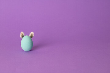 Row of colorful Easter eggs with willow bud ears painted in simple colors on a light purple background - side view with copy space
