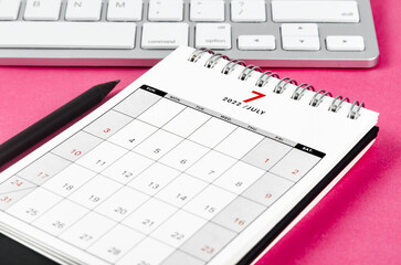 July 2022 desk calendar with pencil on pink background.