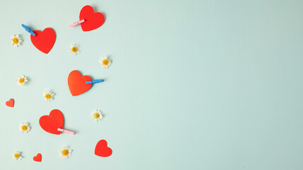 Valentine's Day background. Red hearts, small chamomile flowers on a pastel blue background. Colorful clothespin or colorful clothespin, wooden clips on blue background