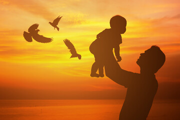 Silhouette of father and child playing at sunset with flying birds.