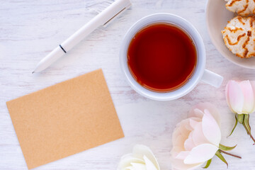 Cup of tea, rose, flowers, coconut macaroons, blank notebook paper, pen over white wooden background. Tea break ideas.