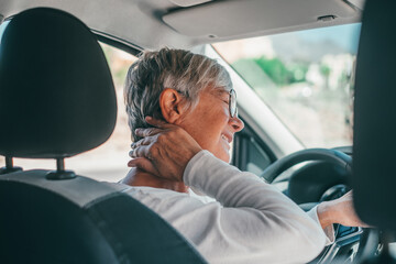 Rear view of old woman having neck pain while driving a car. One senior or mature people feeling bad for injury. - obrazy, fototapety, plakaty