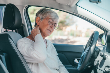 Rear view of old woman having neck pain while driving a car. One senior or mature people feeling bad for injury.. - obrazy, fototapety, plakaty