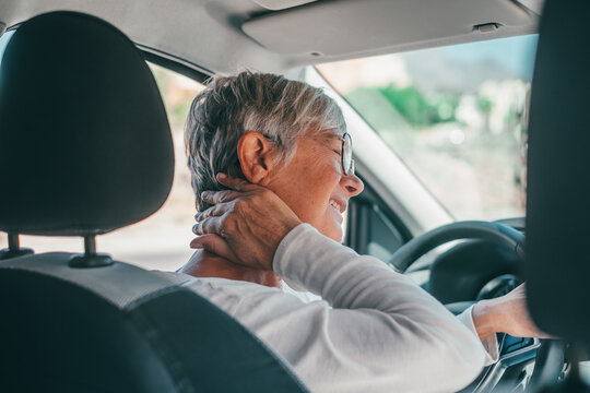 Rear view of old woman having neck pain while driving a car. One senior or mature people feeling bad for injury.