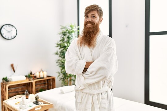 Redhead man with long beard wearing bathrobe at wellness spa happy face smiling with crossed arms looking at the camera. positive person.