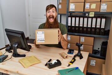 Redhead man with long beard working at small business ecommerce celebrating crazy and amazed for success with open eyes screaming excited.