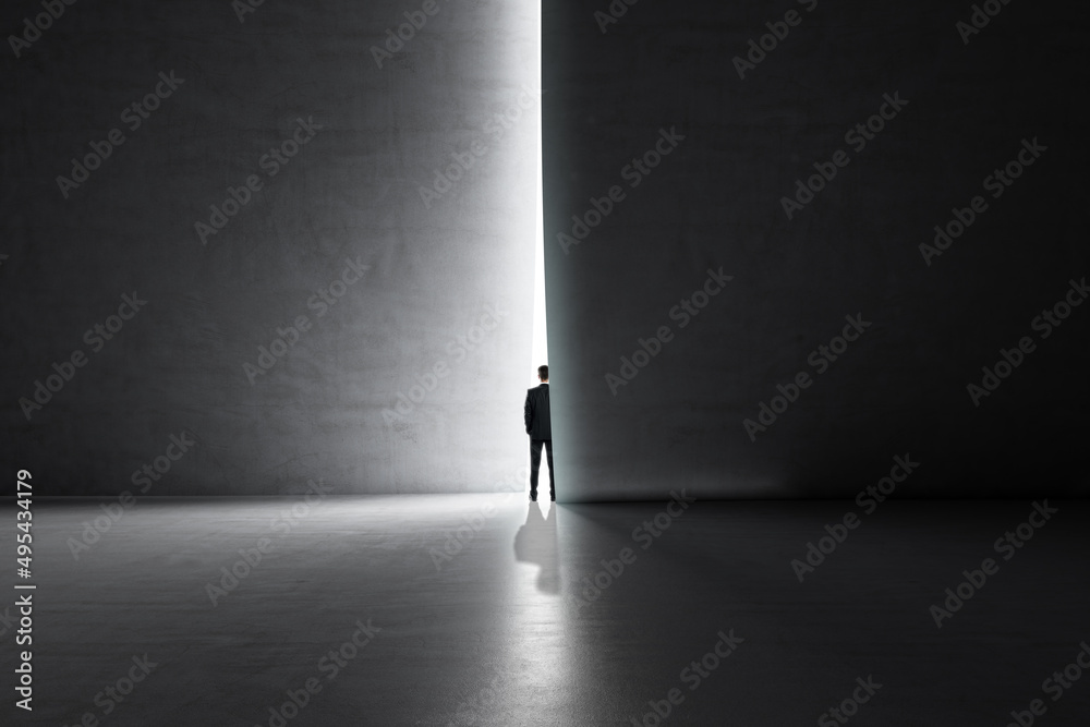 Poster back view of businessman stepping into the light from behind a concrete wall. success and future con
