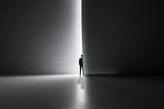 Back view of businessman stepping into the light from behind a concrete wall. Success and future concept.