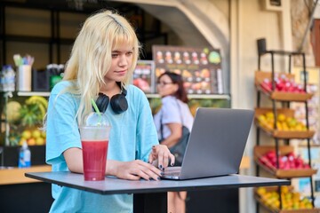 Young woman in outdoor fruit juice bar with fruit fresh juice using laptop