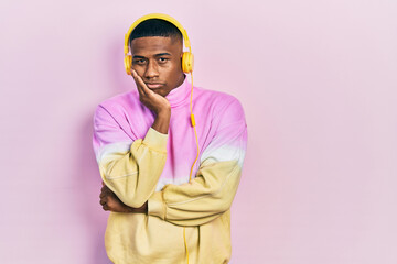 Young black man listening to music wearing headphones thinking looking tired and bored with depression problems with crossed arms.