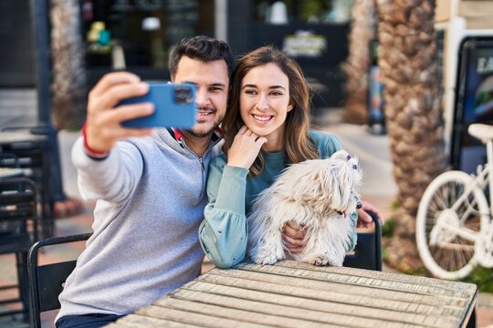 Man and woman holding dog making selfie by the smartphone at coffee shop terrace