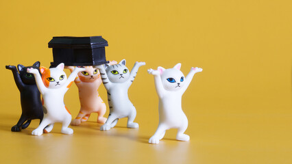 Toy dancing kittens carry a black coffin. Concept of funeral procession dancing with coffin. Yellow...