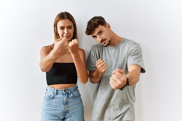 Young beautiful couple standing together over isolated background ready to fight with fist defense gesture, angry and upset face, afraid of problem