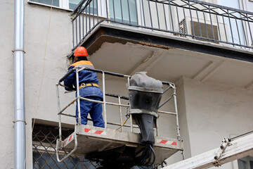 Worker in hydraulic lifting ramp repair the balcony. Builder on lifting platform standing near the...