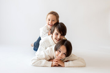 Cute stylish toddler child and older brothers, boys with white shirts on white background, family kids portrait