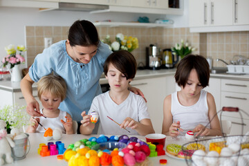 Obraz na płótnie Canvas Three children, sibling brothers, painting easter eggs for decoration, mom helping them