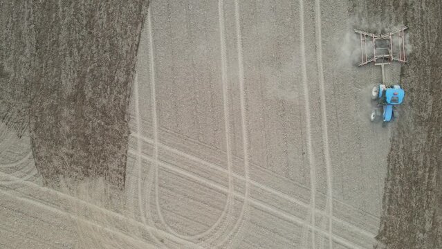 Top down view of farmer discing the field in preparation for planting season. Dry earth creating dust clouds behind the disc. Nice parallel lines in the field.  Then circles around to go back. 