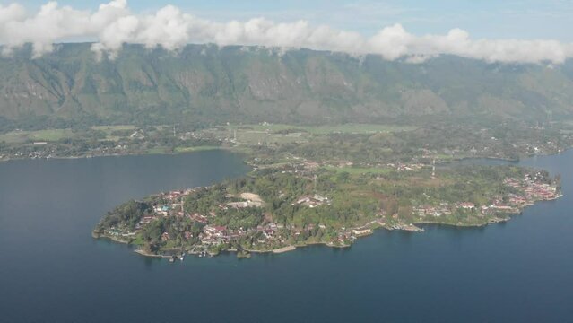 Aerial: flying over lake Toba and Samosir Island Sumatra Indonesia. Tuk Tuk traditional village and tourist destination. Huge volcanic caldera water ecosystem, lush green equatorial forest.