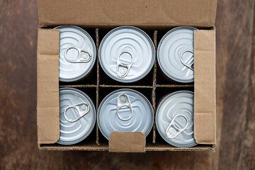 Food cans in a open cardboard box on a wooden table. Concept image for supply chain disruption,...