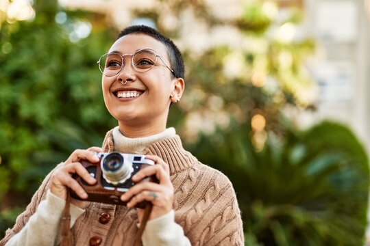Beautiful hispanic woman with short hair smiling happy outdoors holding vintage camera