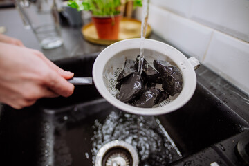 Woman cleaning shungite stones in sieve with pouring water in sink.
