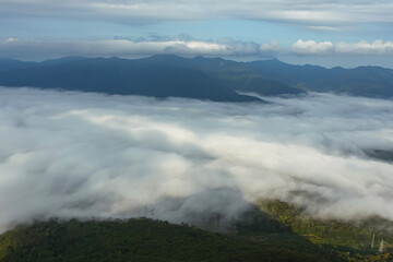 The mountain lowland is covered with fog. In the background are mountain ranges, sky and rain clouds. Beautiful landscape with fog.