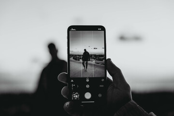 Grayscale photo of hand taking a photo of man