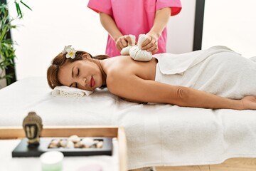 Obraz na płótnie Canvas Young latin woman having back massage session using thai bags