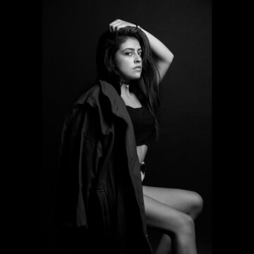 Grayscale photo of young woman in dark coat sitting against dark background