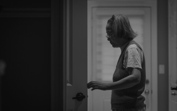 Grayscale photography of older East Asian woman standing beside door