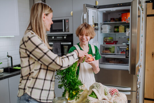 Mother Unpacking Local Food In Zero Waste Packaging From Bag With Help Of Daughter In Kitchen At Home.