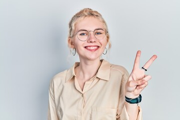 Beautiful caucasian woman with blond hair wearing casual look and glasses showing and pointing up with fingers number two while smiling confident and happy.