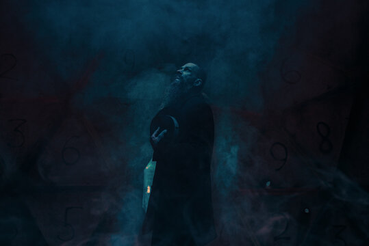 Man in black outfit standing in a dark room looking up