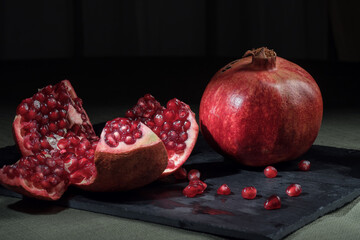 Ripe juicy pomegranate. Pomegranate seeds. Red on black. Still-life. Proper nutrition.
