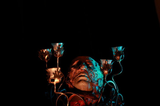 Man's face covered with wax in a candelabra against dark background