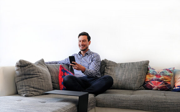 Mature man holding smartphone sitting on couch in living room